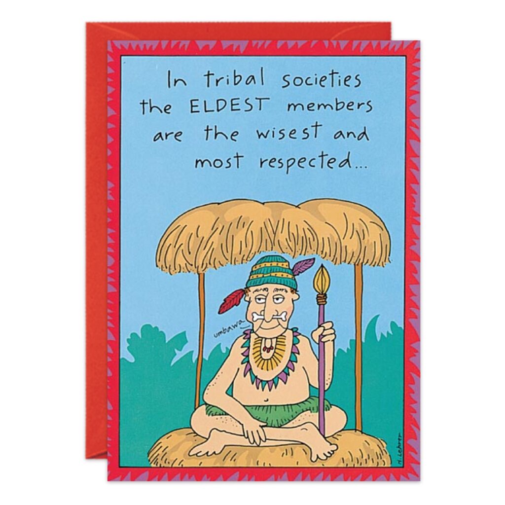 Cartoon of an elderly man with a mustache, feathered headdress, and staff under a thatched hut. Text: In tribal societies, the ELDEST members are the wisest—ideal for an Eldest Birthday Card (1159.jpg).