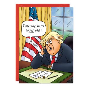 A cartoon man in a suit with blond hair sits at an office desk, holding a phone. A speech bubble says, “They say you’re HOW old?” An American flag and window are behind him. Perfect for a Fake News Birthday Card! Product: 8905.jpg.